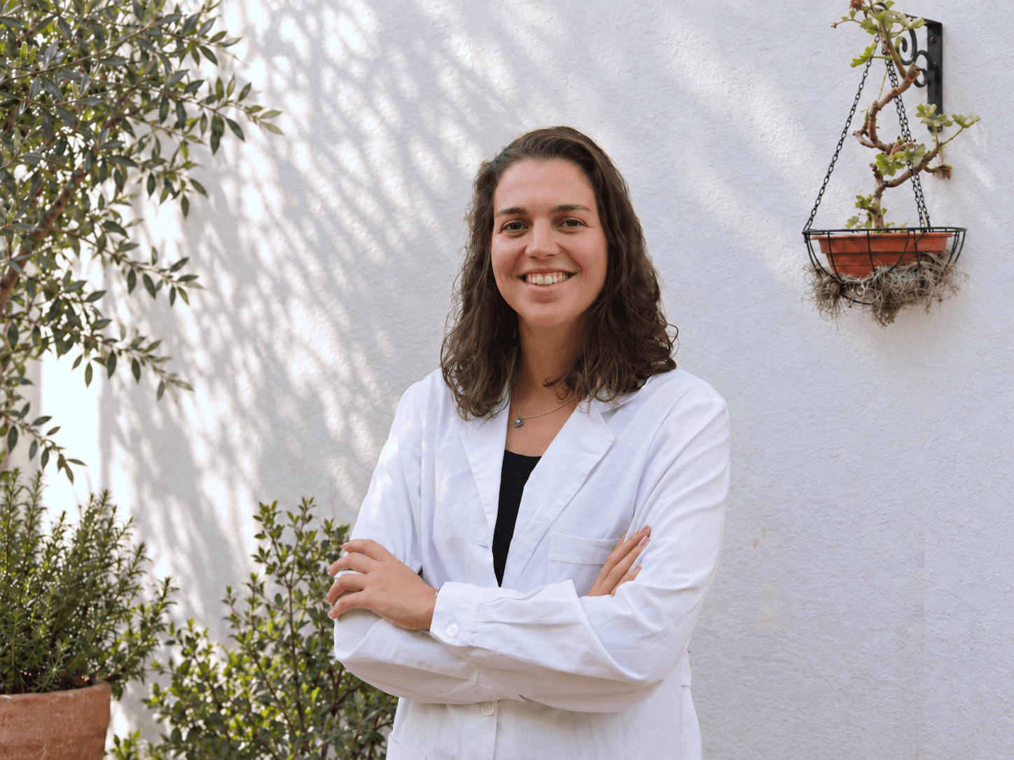 Marta Lucas Santos, nutricionista, de braços cruzados junto a uma parede branca ladeada de plantas.